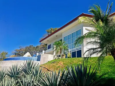 a house on a hill with palm trees in front of it at Modern 4 Bedroom Infinity Pool Beach, Sunset, in Playa Hermosa