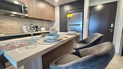 a kitchen with a counter with two chairs and a table at Premium Apartment In Be Cariari in Heredia