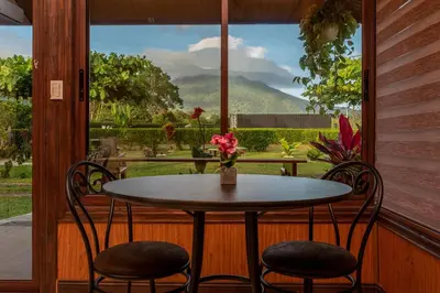 a table and two chairs on a porch with a window at Cabañas Acuarelas del Arenal in Fortuna