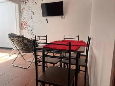 a dining room table with chairs and a television on a wall at Buganvilla Quepos Dos in Tapantí