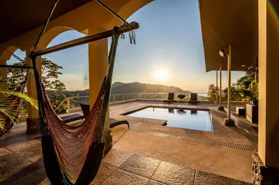 a hammock on the patio of a house with a pool at Villa Cielo in Jacó