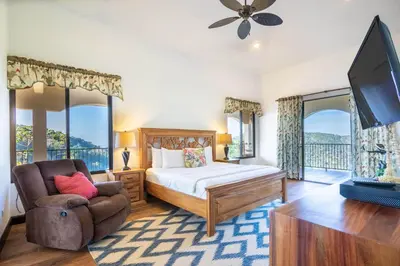 a bedroom with a bed and a chair and a tv at Villa Cielo in Jacó