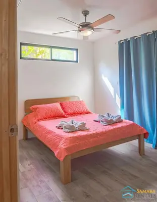 a bedroom with a bed with red sheets and blue curtains at Casa Encanto Charming house 5 minutes walking from the beach in Sámara