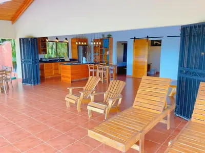 a living room with wooden chairs and a kitchen at Casa Nekori Wonderful Mountain view 15 minutes from Samara in Nicoya