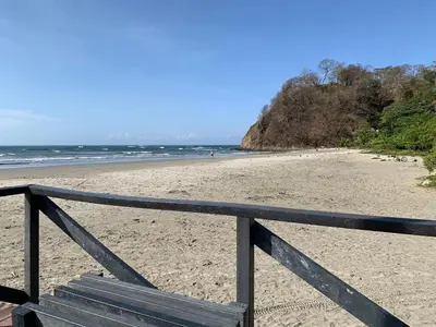 a wooden bench on a beach with the ocean at Oceana Breeze Perfect Getaway steps from the beach in Sámara