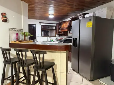 a kitchen with a bar with stools and a refrigerator at Tico Airport B&B in Alajuela City