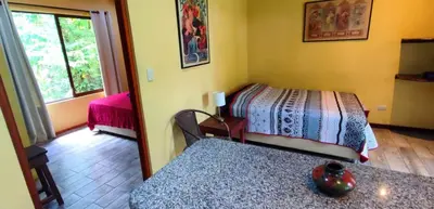 a bedroom with two beds and a table and a window at Villa Colibri at LakeGardens in Nuevo Arenal