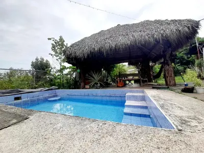 a swimming pool with a straw umbrella and a resort at Casa Rústica Rancho de Lía- Vacacional in Orotina