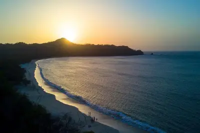 a sunset on a beach with the sun setting over the ocean at The Luxury Condo at Reserva Conchal, Great Beach in Playa Conchal