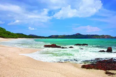 a beach with rocks and the ocean on a sunny day at The Luxury Condo at Reserva Conchal, Great Beach in Playa Conchal
