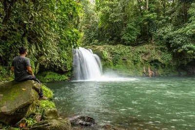 a man sitting on a rock in front of a waterfall at NeyHouse in Sarapiquí
