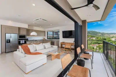 a living room with a white couch and a kitchen at Sol Pacífico at Naumi, Ocean Views & Beach Club in Sardinal