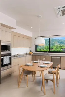 a kitchen with a wooden table and chairs and a window at Sol Pacífico at Naumi, Ocean Views & Beach Club in Sardinal