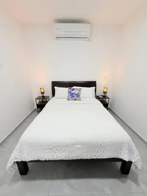 a white bedroom with a white bed with a blue pillow at Casa Azul Jaco in Jacó