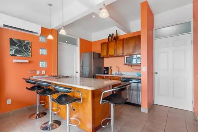 a kitchen with orange walls and a island with bar stools at Modern Top-Floor Condo with Panoramic Views and Community Pool in Coco