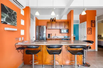 a kitchen with orange walls and a island with bar stools at Modern Top-Floor Condo with Panoramic Views and Community Pool in Coco