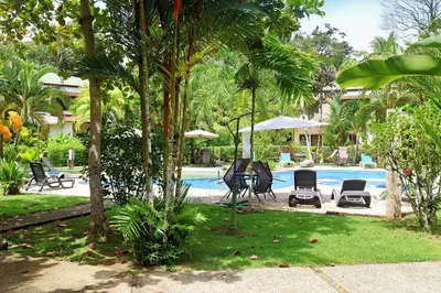 a resort with a swimming pool with chairs and trees at Southern Escapes Apartment in Quepos