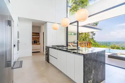 a kitchen with white cabinets and a large window at Casa LaVista - by Pura Villas in Uvita