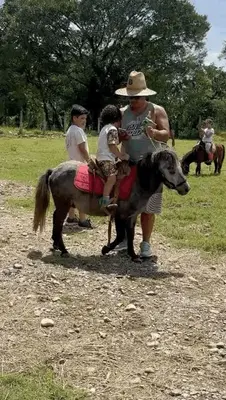 a man with a child riding a pony with a man holding a dog at Tree of Heaven Lodge in San Isidro