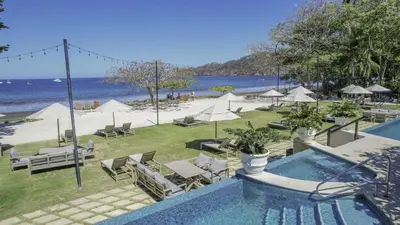 a swimming pool next to a beach with chairs and umbrellas at Brisa del Valle at Naumi, Ocean Views & Beach Club in Sardinal