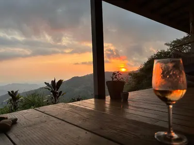 a glass of wine sitting on a wooden table with the sunset at Villa Arcoiris in San Ramón