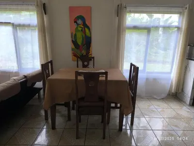 a dining room table with chairs and a parrot painting on the wall at Pacayitas El Camino House in Turrialba