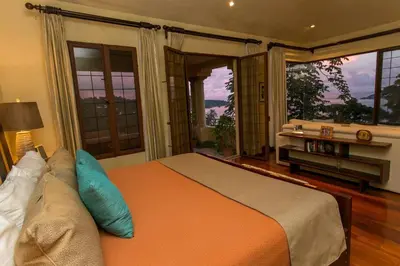 a bedroom with a bed and a couch and windows at Villa Vigia, beach views, 3 acres of privacy and tons of wildlife in Manuel Antonio