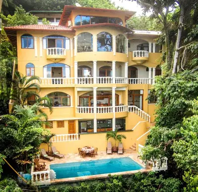 a large yellow house with a swimming pool in front of it at El Capuchin, 2BR Ocean View Apartment, Central Location in Manuel Antonio