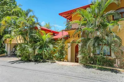a yellow house with palm trees in front of it at El Capuchin, 2BR Ocean View Apartment, Central Location in Manuel Antonio