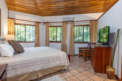a bedroom with a bed and a tv and windows at Jungle Creek all 4 villas up to 19 people in Manuel Antonio