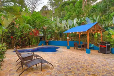 a patio with a table and chairs and a blue umbrella at Casa Pura Vida Manuel Antonio in Manuel Antonio