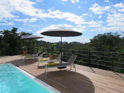 a deck with chairs and an umbrella next to a pool at Monteverde, 1 Bedroom Apartment in La Maison Blanche, Nature in Manuel Antonio