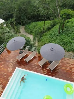 a man in a swimming pool with two umbrellas at Guanacaste, 2 Bedroom Apartment in La Maison Blanche in Manuel Antonio