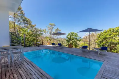 a swimming pool with chairs and umbrellas on a wooden deck at La Maison Blanche Nicoya, Pool, Views, and Wildlife in Manuel Antonio