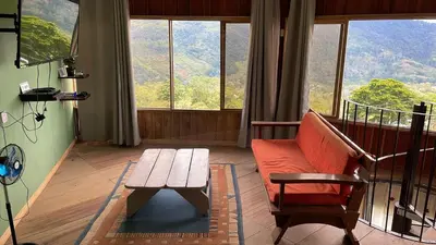 a living room with a couch and a table and windows at Cabaña El Mirador de las Montañas in Turrialba