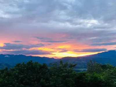 a sunset in the mountains with trees in the foreground at Cabaña El Mirador de las Montañas in Turrialba