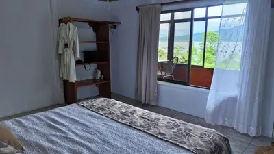 a bedroom with a bed and a window with a chair at Volcano & Lake Arenal View Suite with Soaking tub in El Castillo de La Fortuna