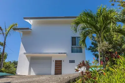 a white house with a palm tree in front of it at Lapa Roja, 2BR Ocean View Apartment in Villa Mar y Sol, Nature in Manuel Antonio