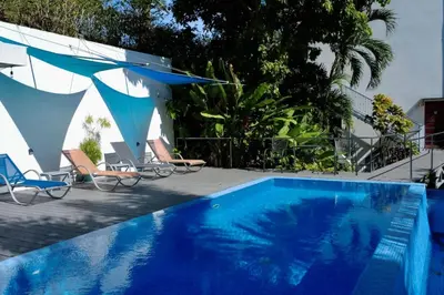 a blue swimming pool with chairs and umbrellas at Lapa Roja, 2BR Ocean View Apartment in Villa Mar y Sol, Nature in Manuel Antonio