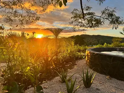 a garden with a sunset in the background at Refugio del Ocaso - neues Teak-Haus mit Garten in Hojancha