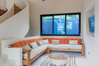 a living room with an orange couch and two windows at Nakama Nosara in Nicoya