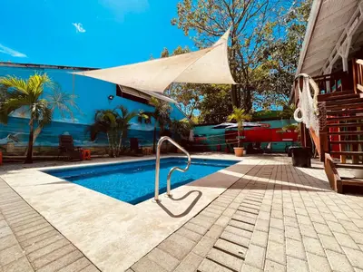 a swimming pool with a tan umbrella next to a house at Blue Iguana in Sámara