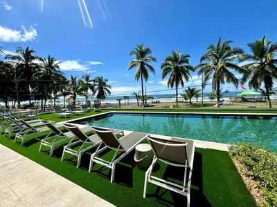 a row of lawn chairs in front of a swimming pool at Serene and Modern Beachfront Condo with Ocean Views in Jacó