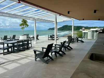a patio with tables and chairs and a view of the ocean at Serene and Modern Beachfront Condo with Ocean Views in Jacó