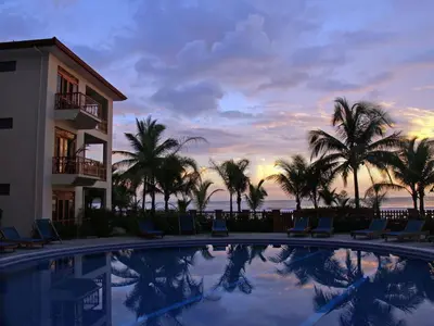 a swimming pool with palm trees and a building at Bahia Azul 3A in Jacó