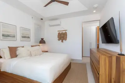a white bedroom with a bed and a flat screen tv at Salty Living - Tamarindo Hills in Tamarindo