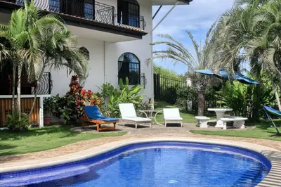 a swimming pool in front of a house with two chairs at Casa Mimosa Buenavista in Playa Flamingo