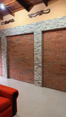 two garage doors on a brick wall with a red couch at Green Shelter in Quepos