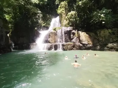people swimming in the water in front of a waterfall at La Ceiba Ecoadventures Wildlife Reserve in Platanillo