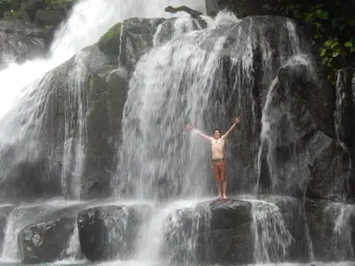 a man standing on a rock in front of a waterfall at La Ceiba Ecoadventures Refugio de vida silvestre in Platanillo
